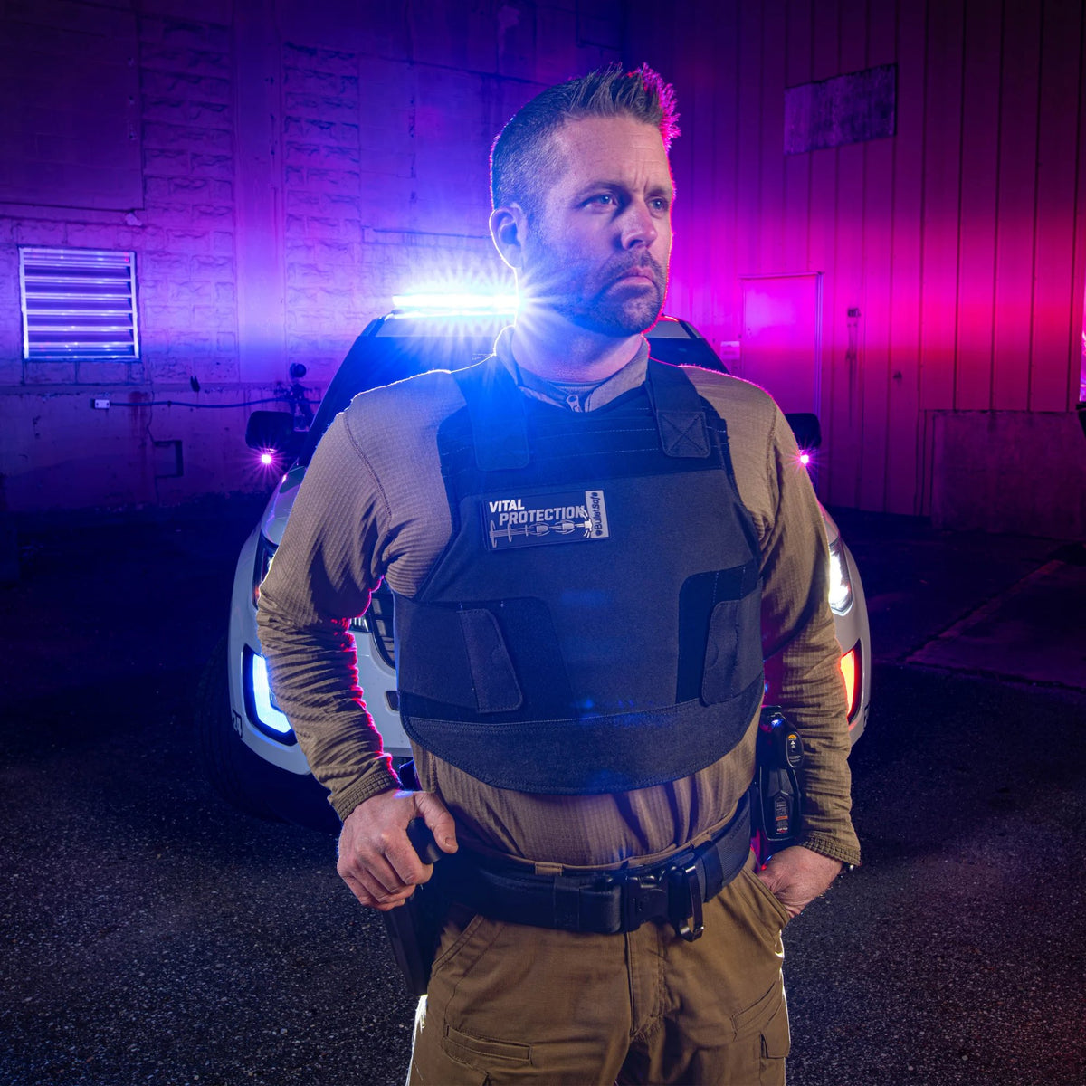 Police officer in a BulletSafe vest beside a patrol car with its lights on